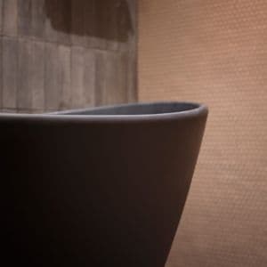 Sort badekar med rosa fliser på vegg kombinert med grå